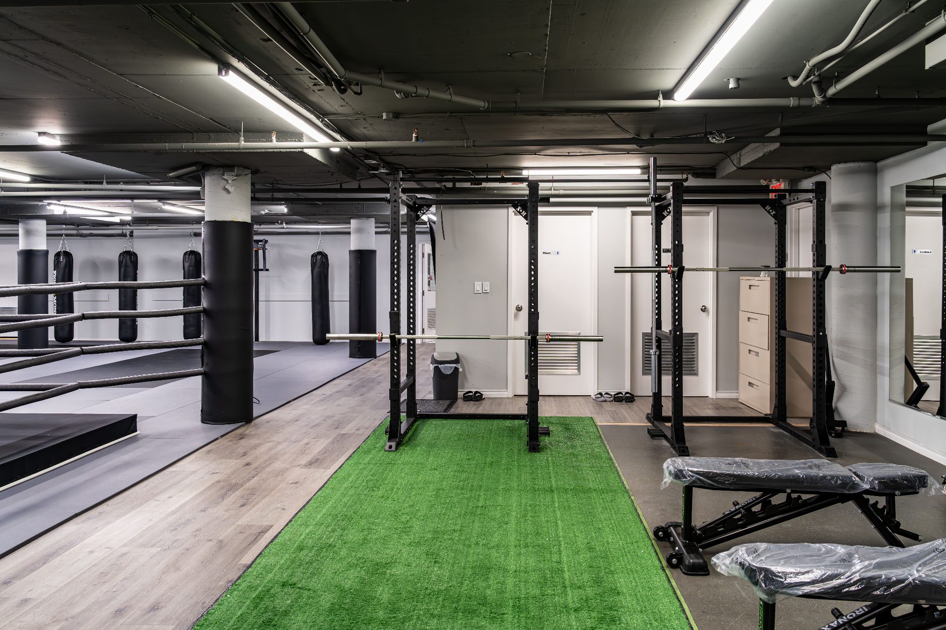 Squat racks with barbells on turf strip beside the heavy bag area